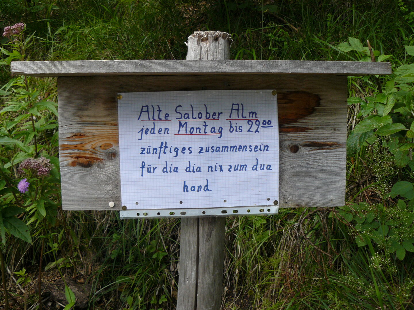 The sign reads "Old Salober Alp (=name of the hut), every Monday until 10 p.m. traditional get-together for people who have nothing to do", written in Bavarian dialect.