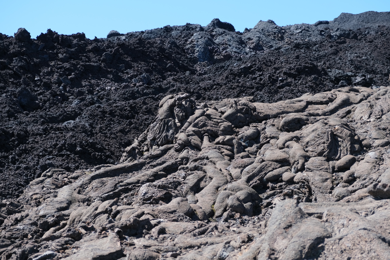 Verschiedene Arten Lava: vorne die Pahoehoe-Lava mit glatter Oberfläche, hinten die raue A-a-Lava. Die Goldfäden heißen Pele-Haar und sind aus Glas. 