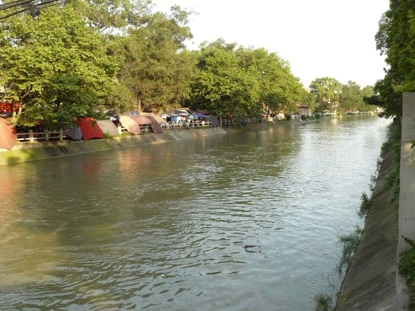 The river flowing next to the campus. The old part of the campus is on the right; if you go along the left side of the river you reach the new campus. The water is brownish with a lot of trash floating in it.